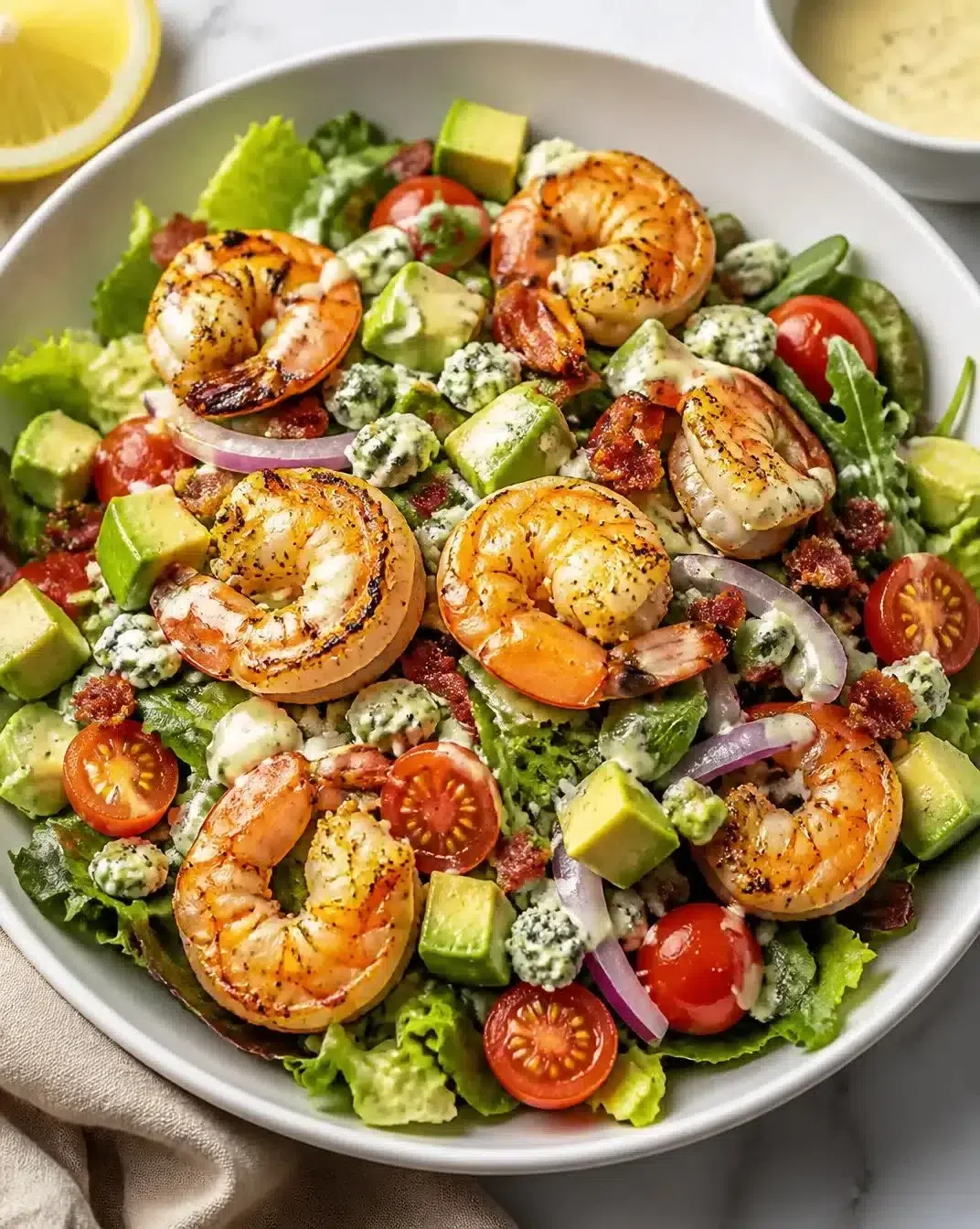 Charred shrimp cobb salad with greens, avocado, and dressing on a plate.
